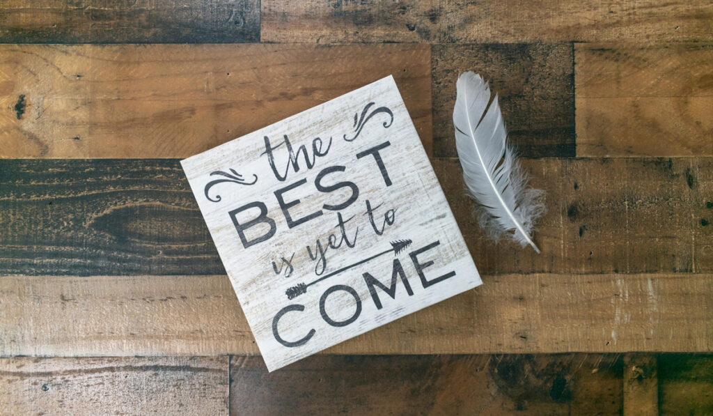 The best is yet to come sign with feather on side on wooden background