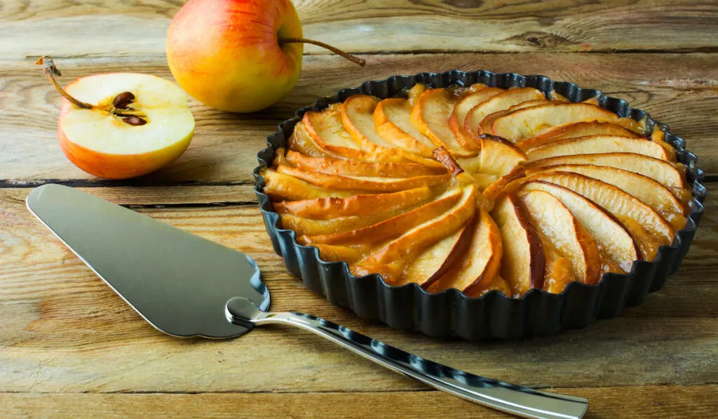 Traditional apple pie with fresh apples on pie pan and wooden table