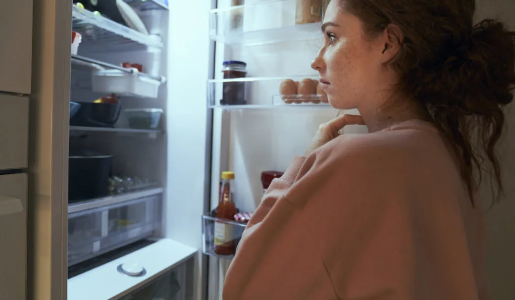 Undecided young woman checking food from the fridge