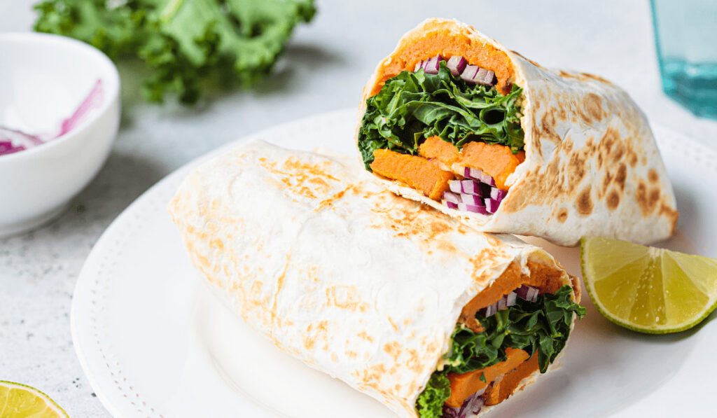 Vegan burrito wrap with sweet potato, kale and onion in white plate 