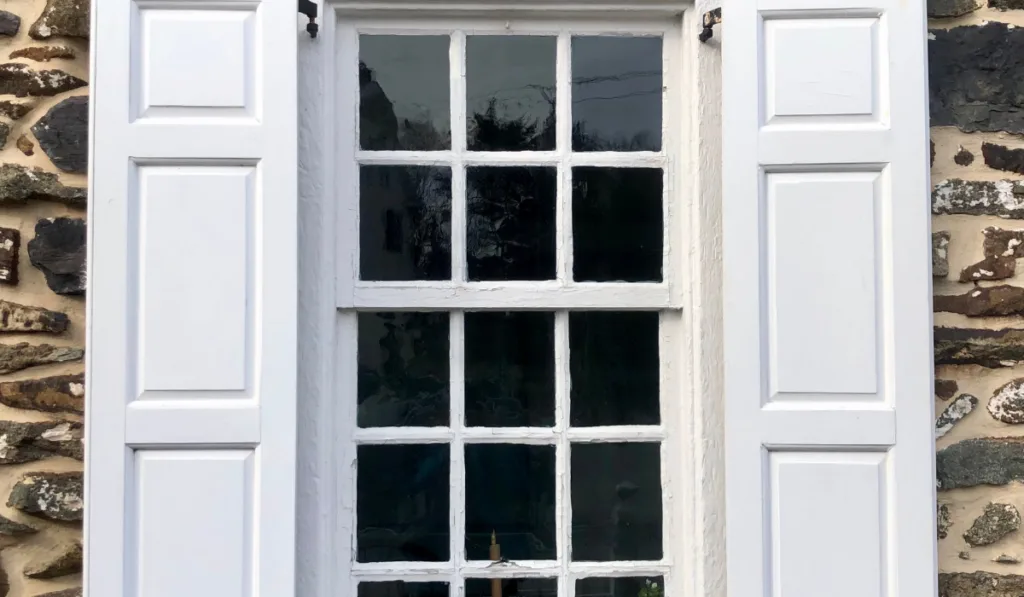 White window shutters in window in stone house
