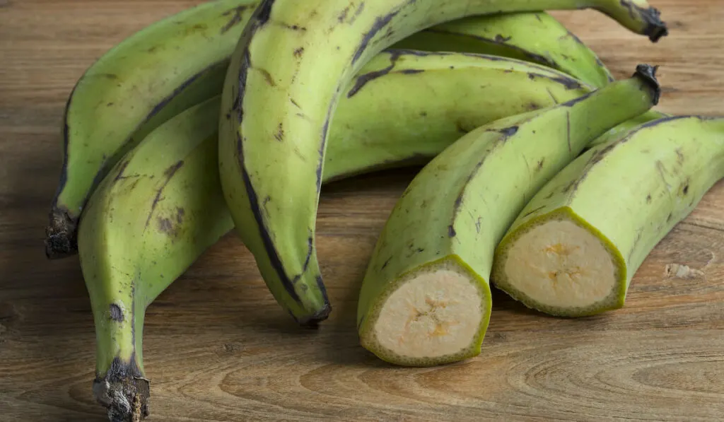 Whole and half green unripe bananas on wooden table