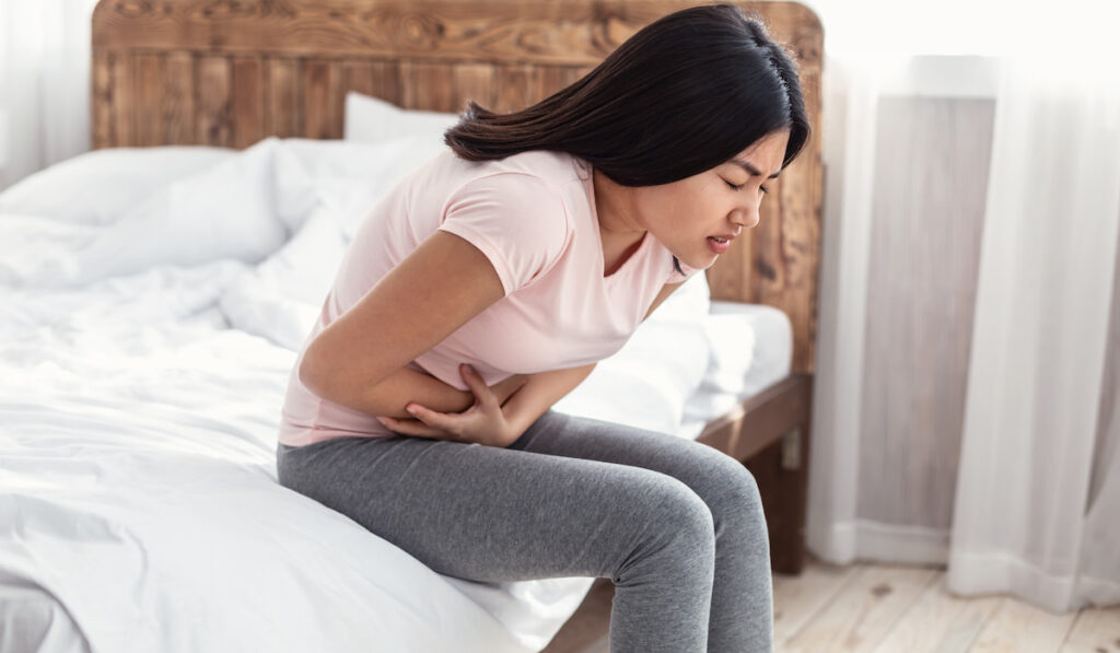 Woman Having Stomachache Suffering From Pain Sitting At Home