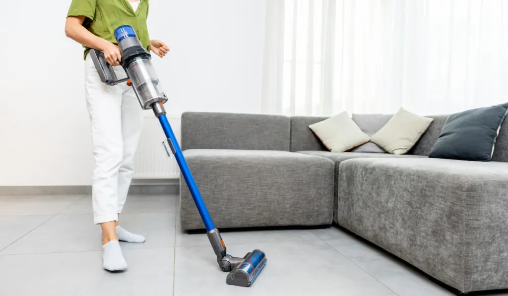 Woman cleaning floor tiles with cordless vacuum cleaner 