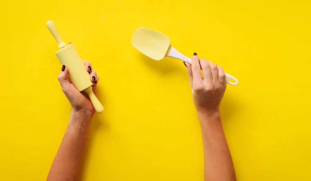 Woman hand holding rolling pipn and spatula  on yellow background