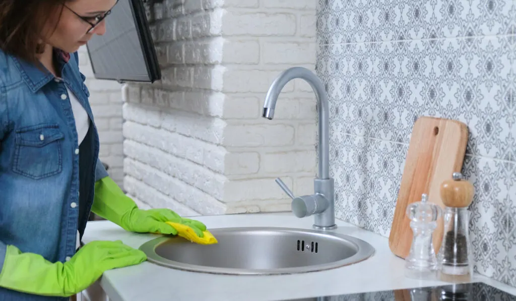 Woman wearing gloves  washing cleaning polishing kitchen metal sink
