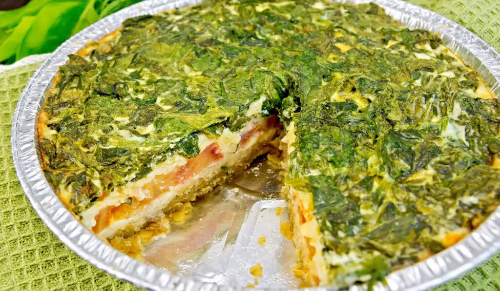 baked pie with spinach and tomatoes in foil pie pan