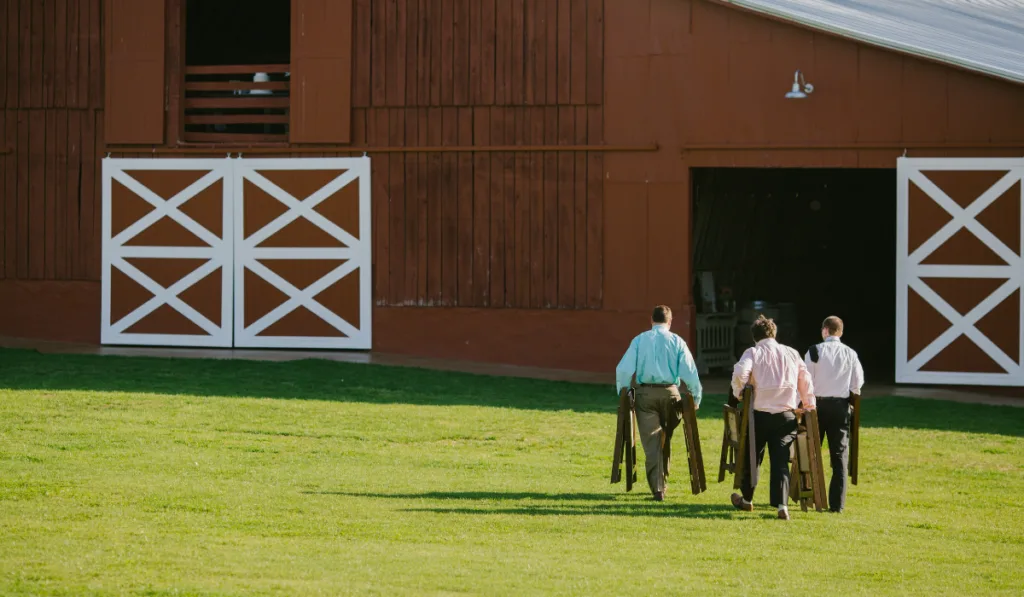 three men walking into a barn carrying foldable tables