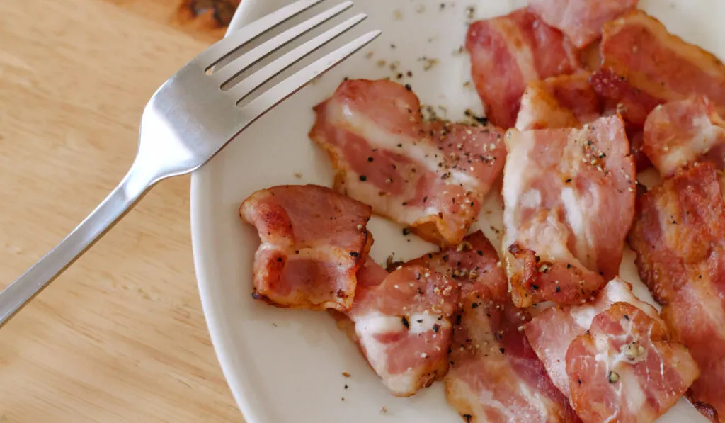 cooked bacon in white plate with fork