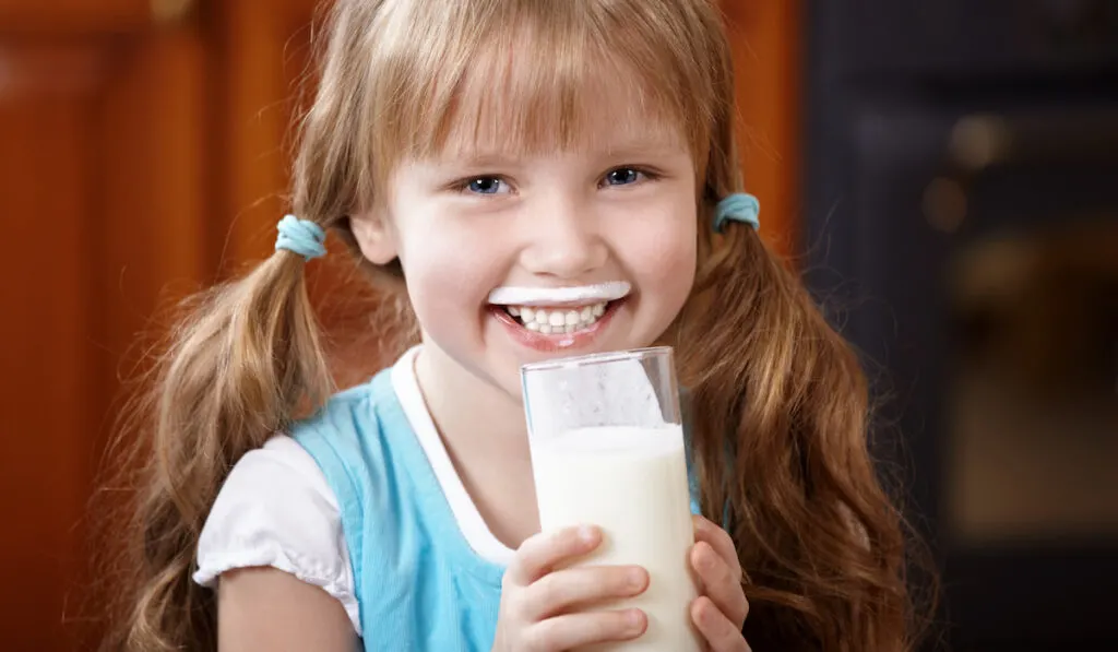 cute little girl drinking milk in a glass 
