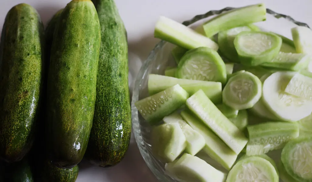 fresh whole and sliced cucumbers on glass bowl 