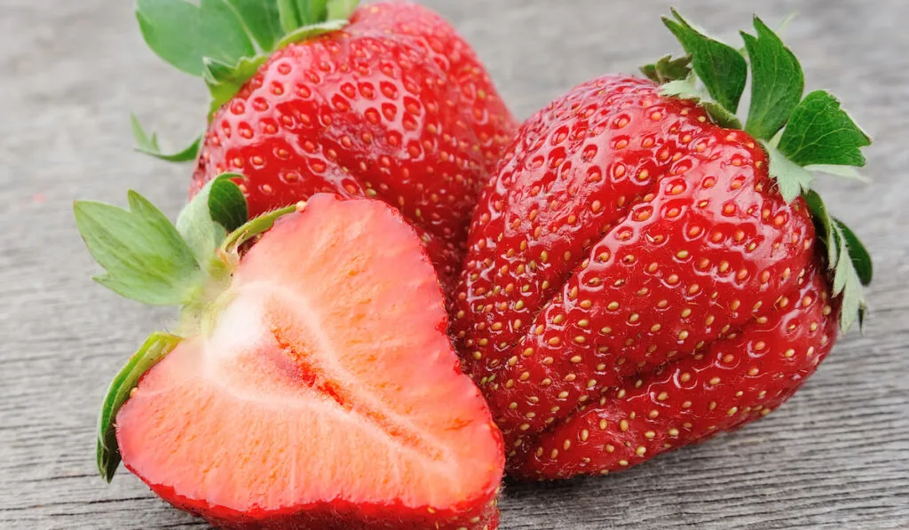 fresh whole and sliced strawberries on wooden background 