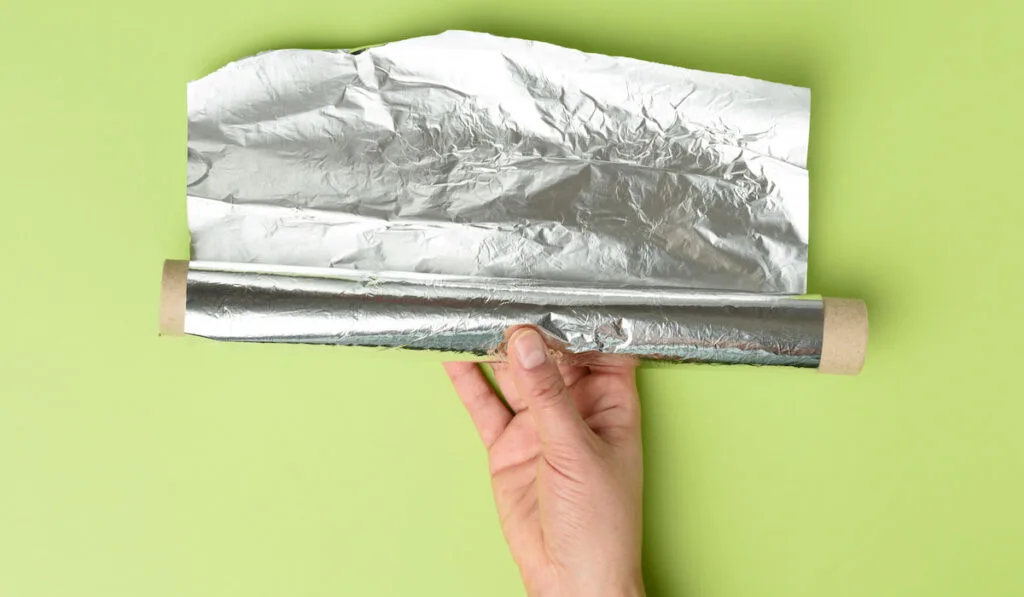 hand holding aluminum silver foil on green background