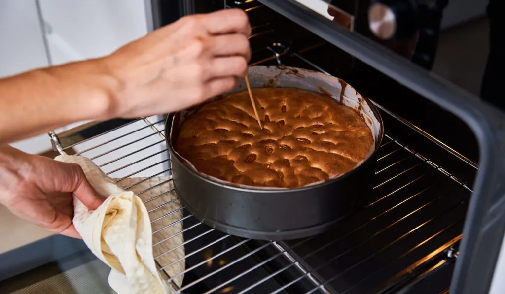 lady checking bake cake in baking pan from oven