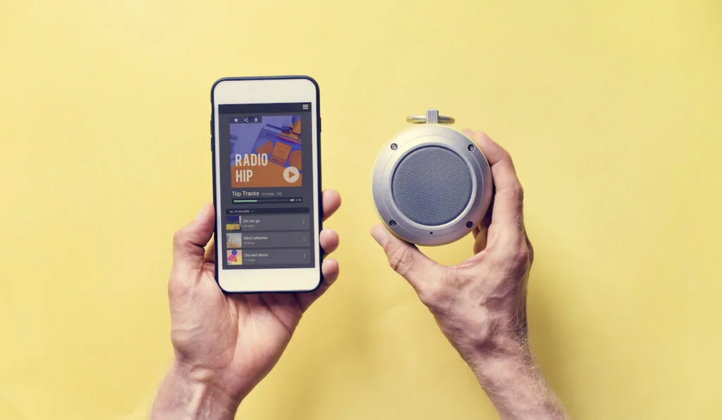 man holding phone and bluetooth speaker plays music