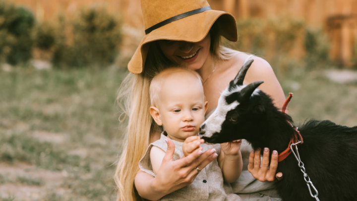 portrait-of-smiling-mother-in-hat-and-little-son-petting-domestic-goat-at-countryside