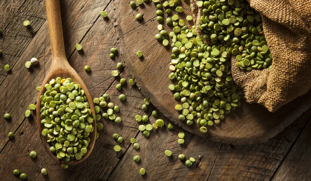 raw green split peas on wooden board and spoon 