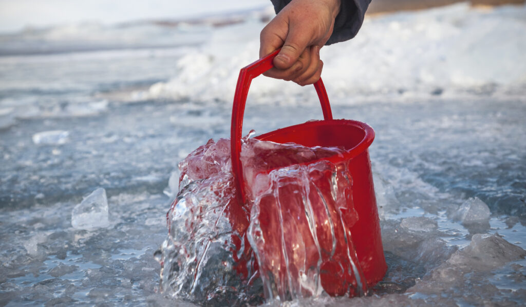red water bucket getting water from frozen lake 