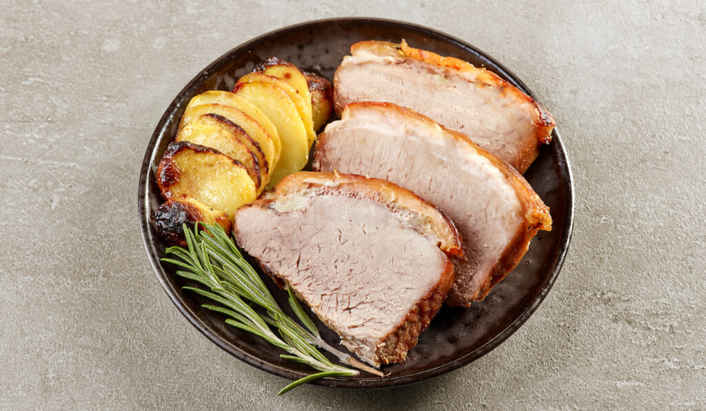 roasted pork slices with herb and potatoes on black plate