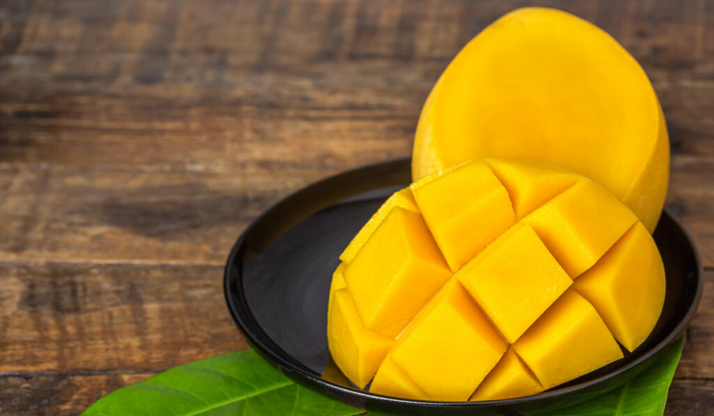 slice of ripe mango on black plate with leaves