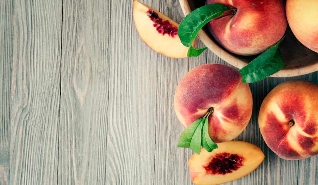 sliced and whole peaches on wooden table 