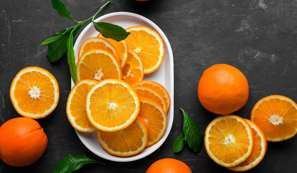 sliced oranges in white plate and whole oranges on black background
