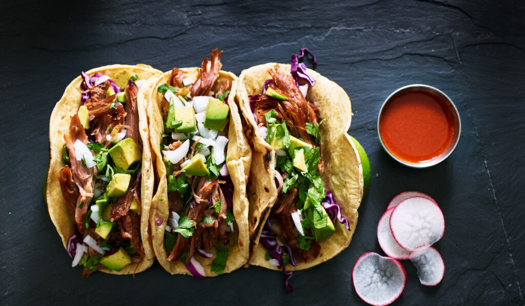 three mexican pork carnitas tacos on black background 