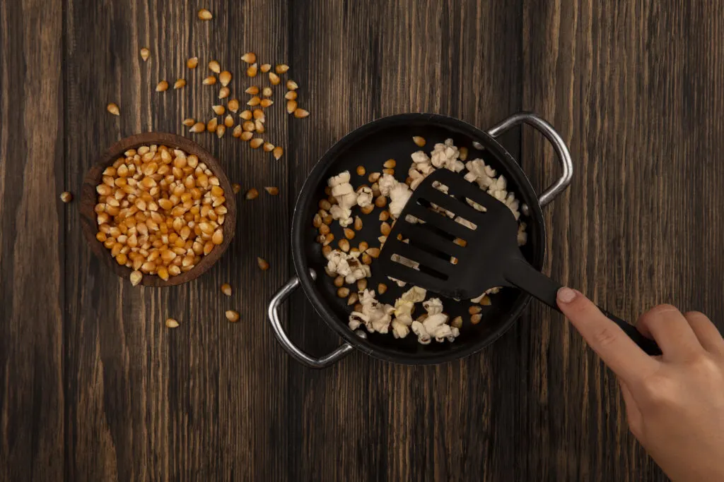 top view if woman holding slotted spatula tuner over pan with popcorns 