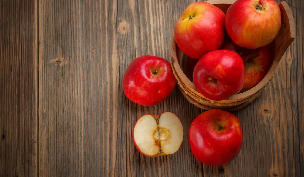 whole and sliced red apples on wooden background