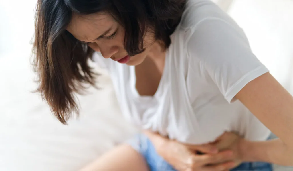 woman having stomachache sitting on white sofa 