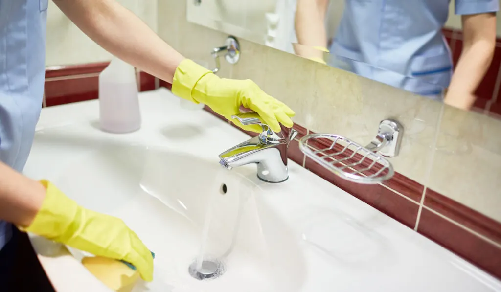 woman on uniform cleaning bathroom sink 
