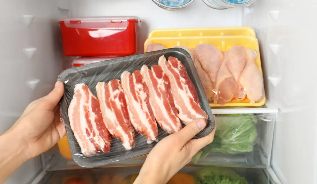 woman taking raw bacon from the refrigerator