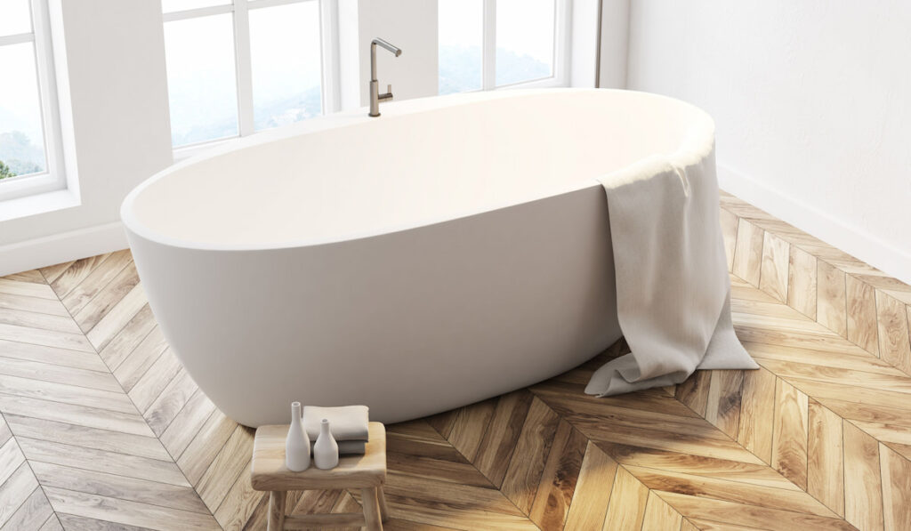 Minimalistic bathroom interior with tall windows, white walls, a wooden floor and a white porcelain bathtub