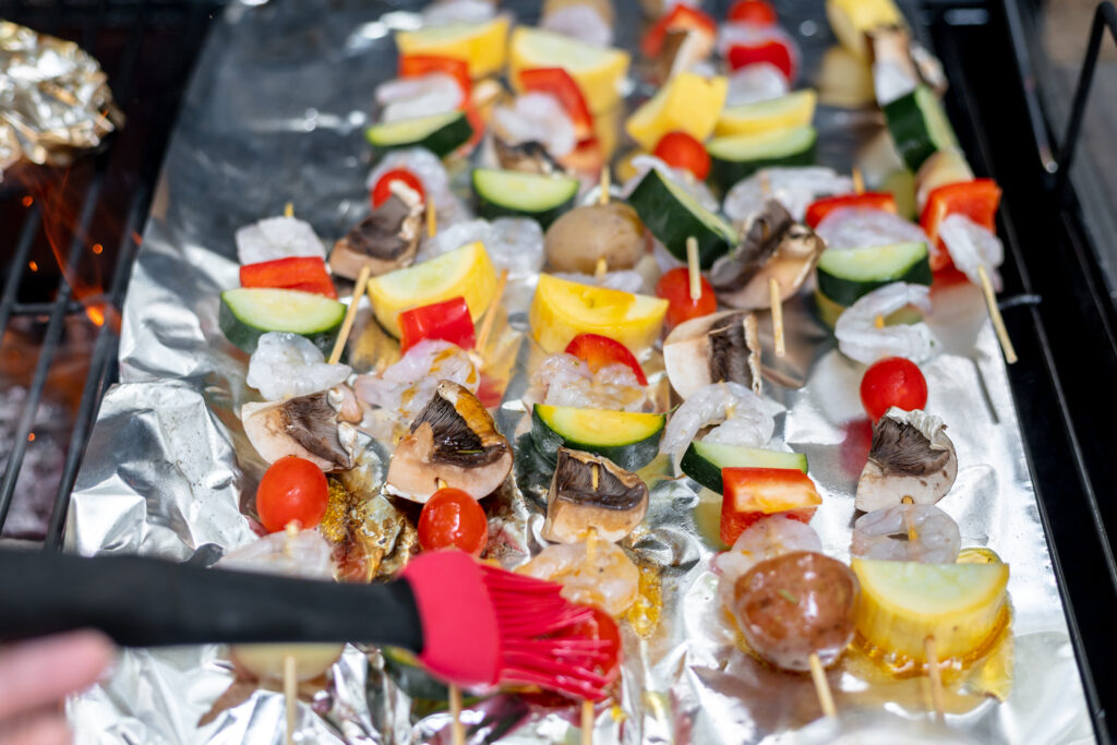 basting the shrimp and veggies skewers with olive oil 