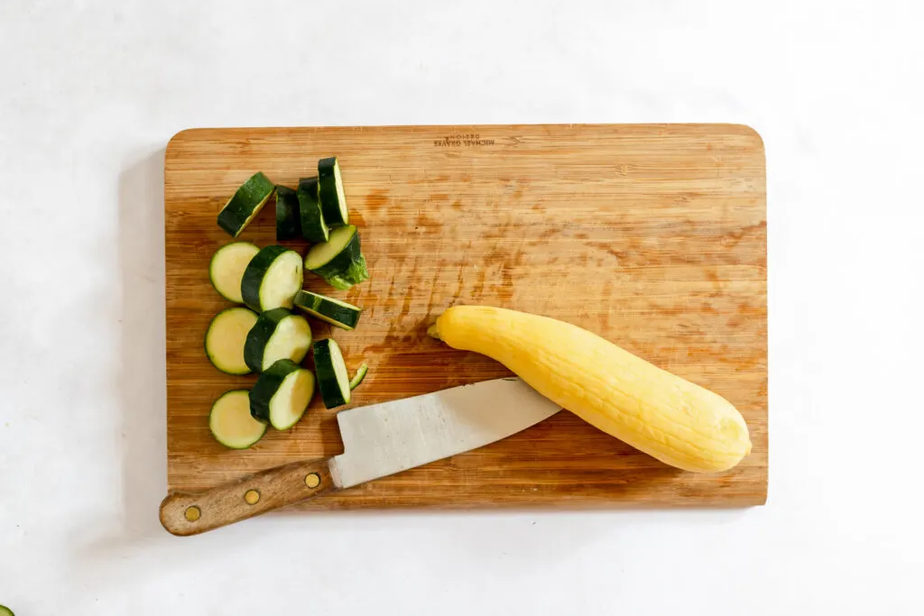 whole and sliced zucchinis on chopping board with knife