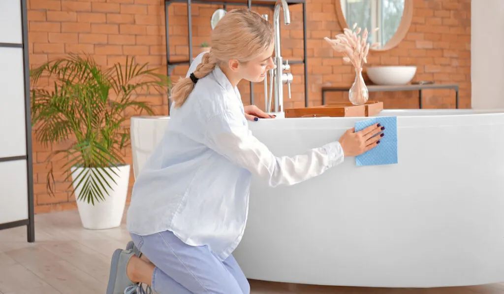 Young woman cleaning bathtub in bathroom 