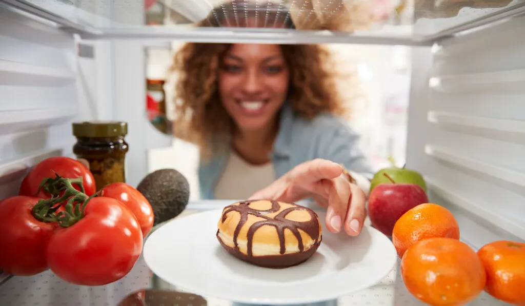 woman getting donut on a plate inside the fridge