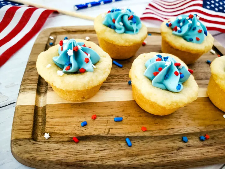 pretty sugar cookie cups with blue frosting arranged neatly on a wood cutting board with red and white sprinkles