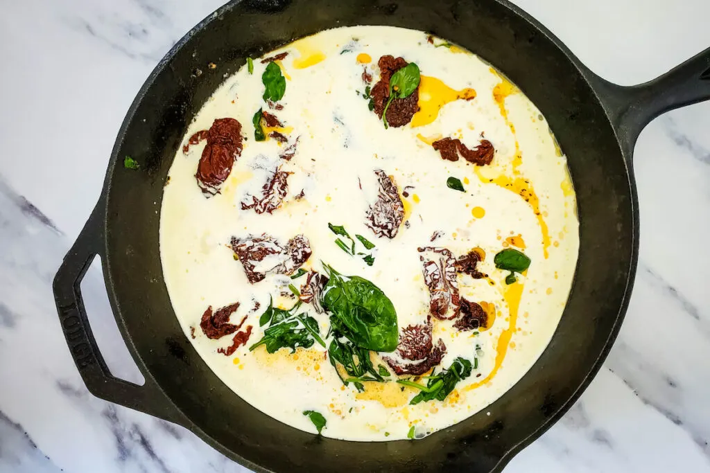 Cream and milk with sun-dried tomatoes and spinach in a cast iron skillet