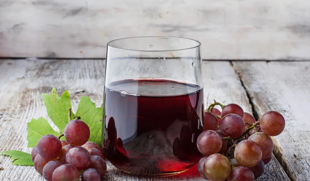Glass of fresh grape juice and fresh grapes on a rustic table
