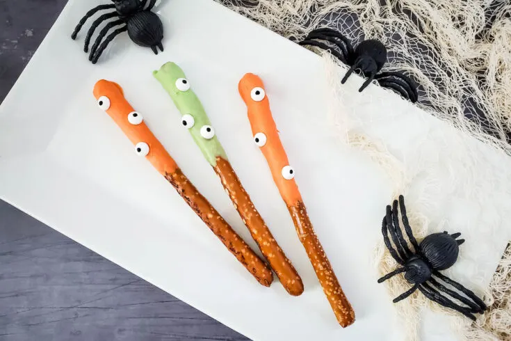 Halloween Monster Pretzels with colorful dip on white rectangular plate with black spiders and spider web on the side