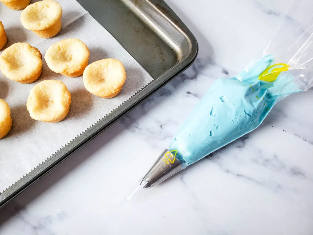 Prepared pipping bag with frosting beside a tray of freshly baked cookie sugar cups