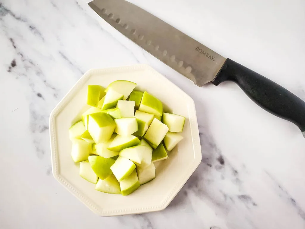 diced apple on a white plate and a knife on the side laid on marble table