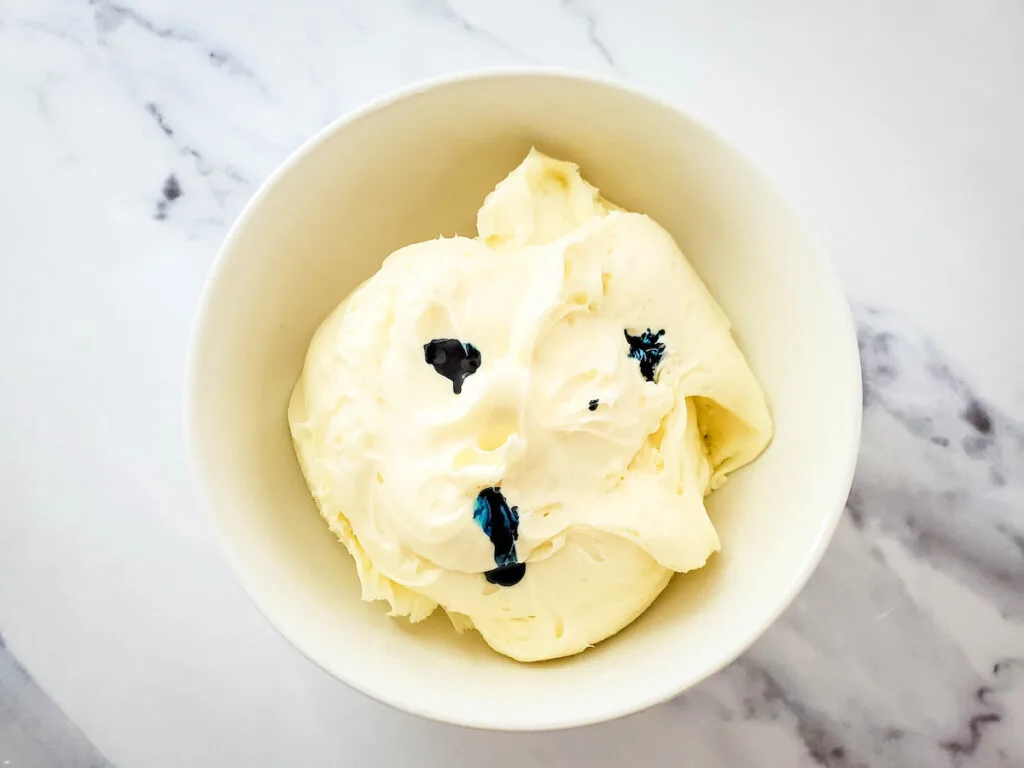 drops of blue food coloring on the bowl of frosting