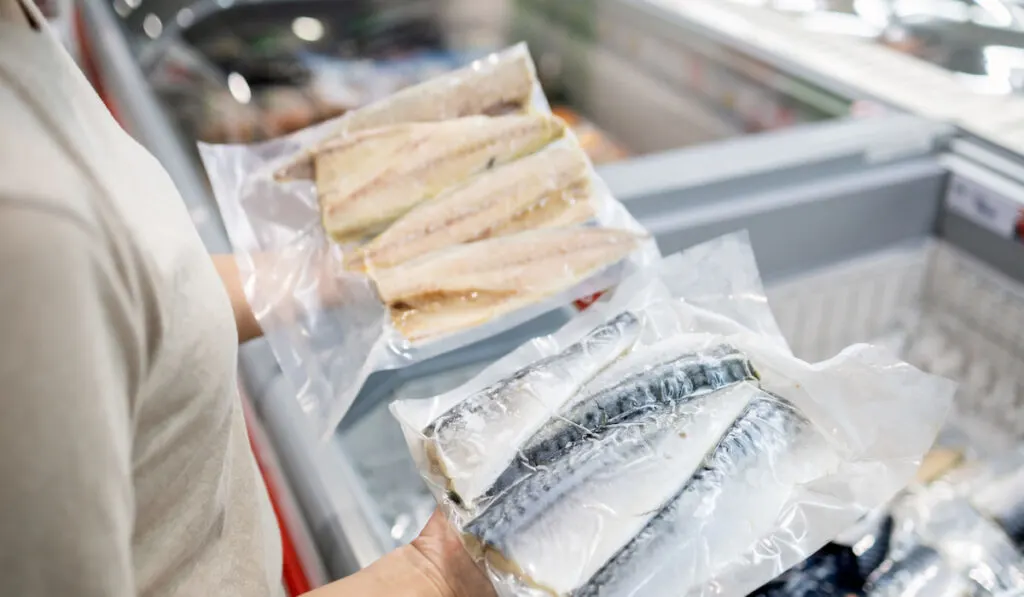  woman wear face mask, choosing packed frozen cut fish in freezer in food department of supermarket