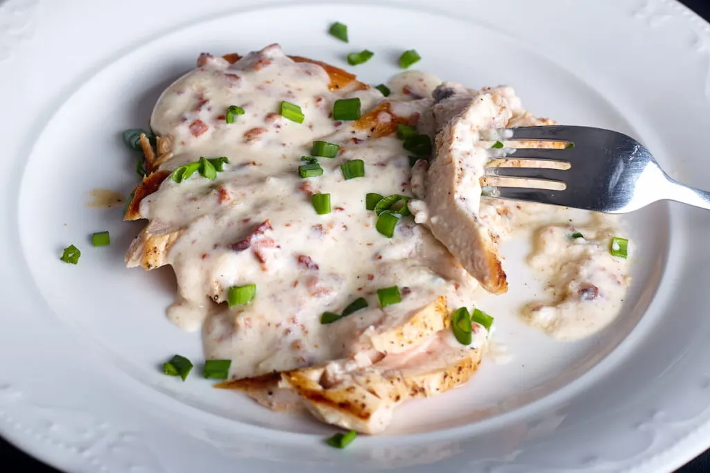 Close up of grilled chicken breast under the alfredo sauce.
