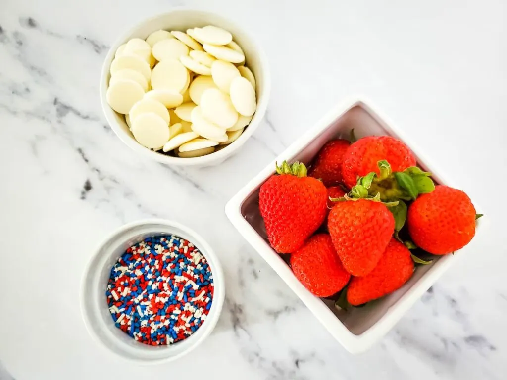 Ingredients for patriotic white chocolate coated strawberries prepared on top of a marbled table 
