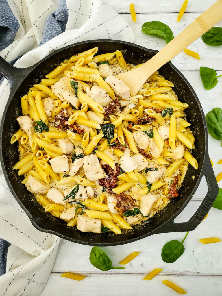 freshly cooked Tuscan chicken pasta in a cast iron skillet, with wooden spoon on the table