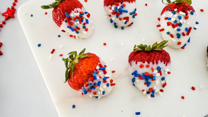 six-pieces-strawberries-coated-with-white-chocolates-and-red-blue-sprinkles-on-white-plate-on-marble-table