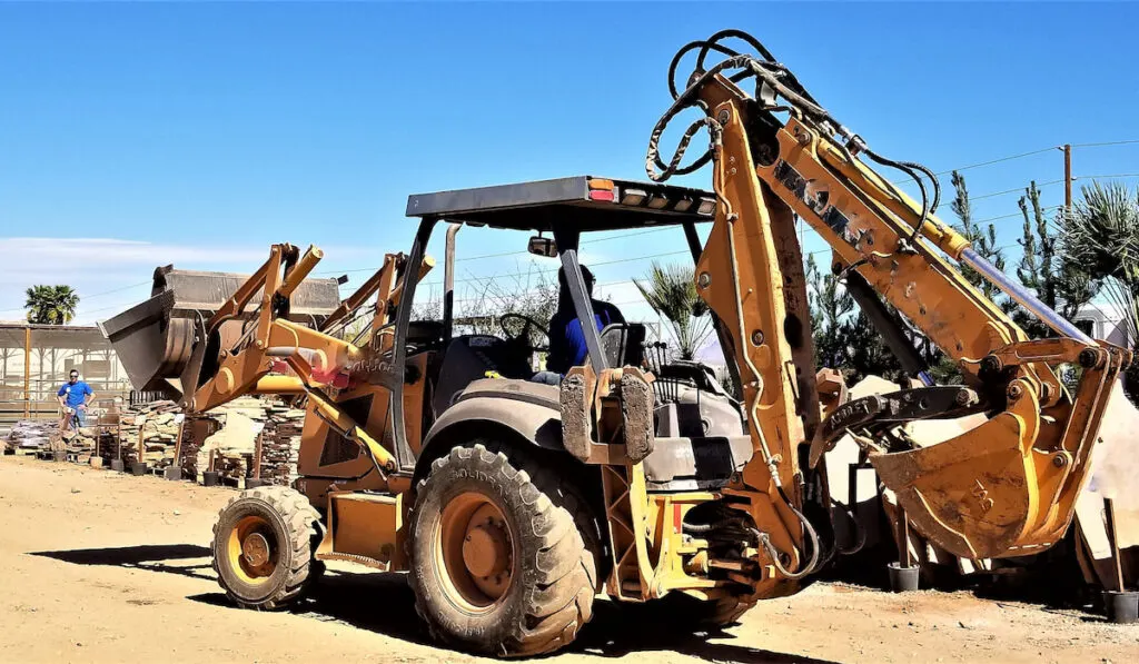 A worker directs the driver of the backhoe loader to the gravel truck to dump on a construction site